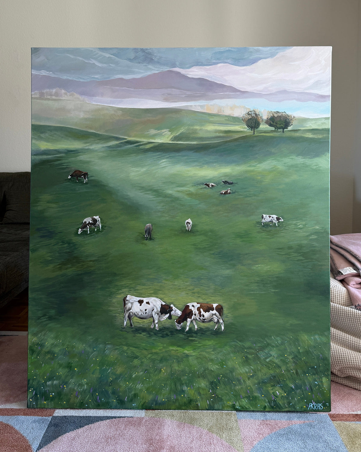Painting of cows grazing in a green field with mountains in the background